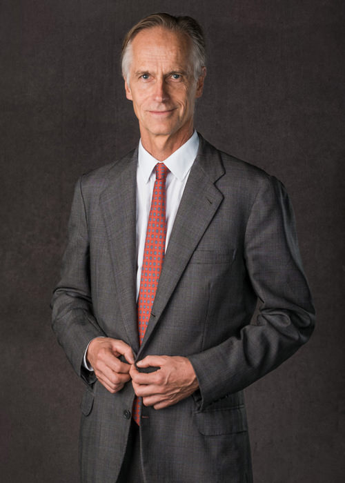 A 3/4 length corporate portrait of a middle aged man wearing a grey suit and red tie
